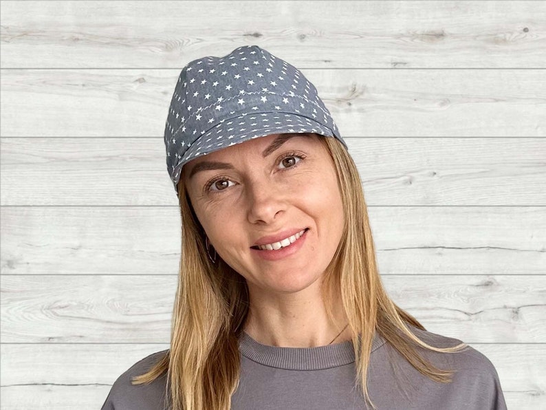 K&ouml;nnte beinhalten: Eine Frau mit langen blonden Haaren tr&auml;gt eine blaue und wei&szlig;e Kappe mit Sternenmuster. Die Kappe hat ein gebogenes Visier und eine flache Oberseite. Die Frau l&auml;chelt und schaut in die Kamera.