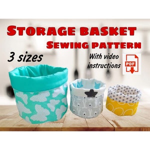 May include: Three fabric storage baskets in different sizes and patterns. The largest basket is turquoise with a white butterfly pattern, the medium basket is gray with a white elephant pattern, and the smallest basket is yellow with a gray star pattern. The text "STORAGE BASKET SEWING PATTERN" is at the top of the image, and the text "3 sizes" is below it. The text "With video instructions" is on the right side of the image, and a PDF download icon is next to it.