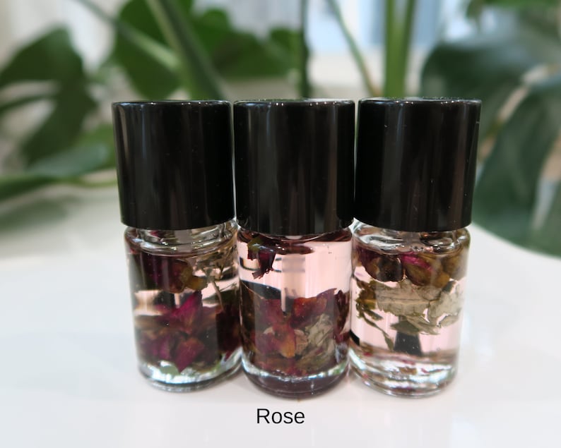 May include: Three small glass bottles with black lids filled with clear liquid and dried rose petals. The bottles are labeled "Rose".