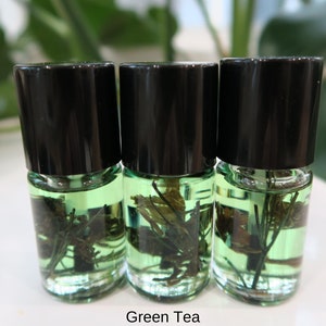May include: Three small glass bottles with black lids filled with a green liquid and green plant matter. The bottles are labeled "Green Tea".