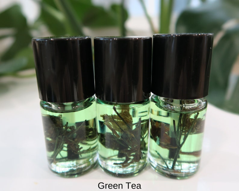 May include: Three small glass bottles with black lids filled with a green liquid and green plant matter. The bottles are labeled "Green Tea".
