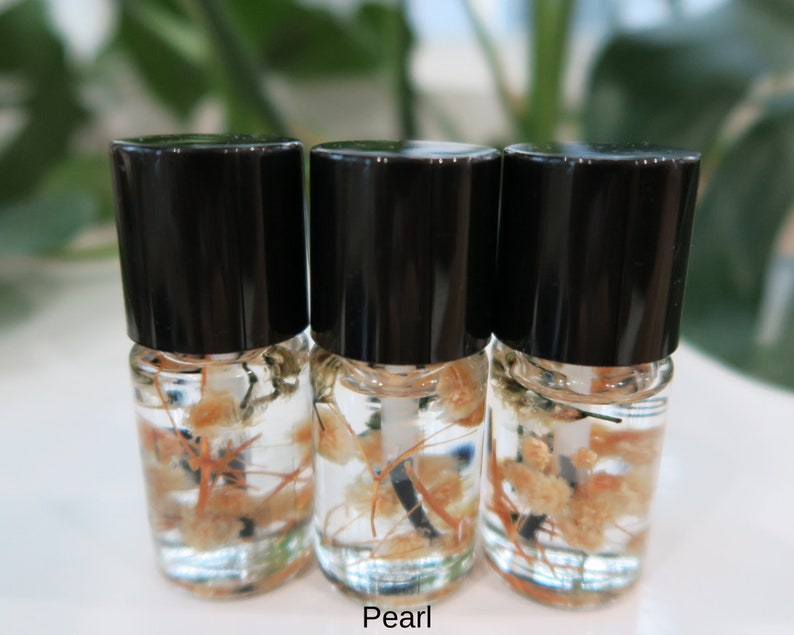 May include: Three small glass bottles with black caps filled with a clear liquid and dried flowers. The bottles are labeled "Pearl".