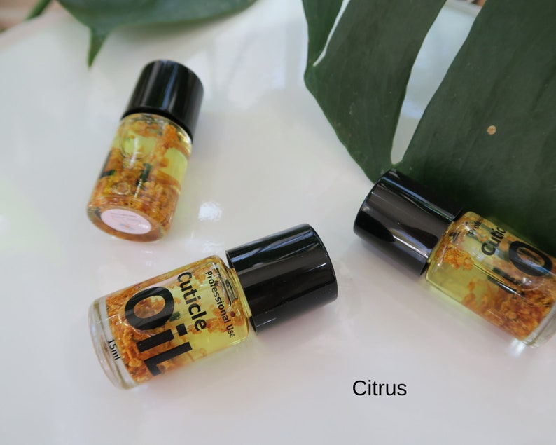 May include: Three small bottles of cuticle oil with black caps and clear glass bottles filled with a yellow liquid and small yellow flower petals. The bottles are labeled "Cuticle Oil" and "Professional Use". The text "Citrus" is written below the bottles.