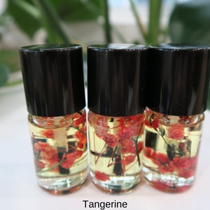 May include: Three small glass bottles with black caps filled with a yellow liquid and red and white dried flowers. The bottles are labeled "Tangerine".