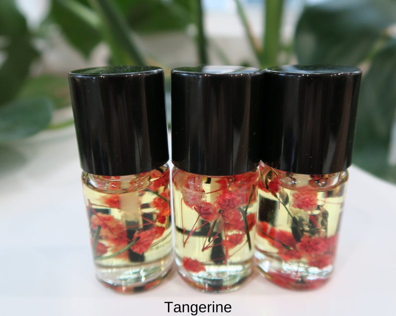 May include: Three small glass bottles with black caps filled with a yellow liquid and red and white dried flowers. The bottles are labeled "Tangerine".