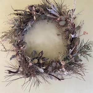 May include: A dried floral wreath made with various types of greenery, including eucalyptus, pine, and other dried foliage. The wreath is a natural, rustic, and earthy design.
