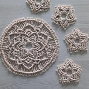 Könnte beinhalten: Fünf Makramee-Untersetzer in Cremefarbe. Die Untersetzer sind in Form von Sternen und Kreisen. Die Untersetzer sind aus dickem, geknotetem Seil gefertigt.