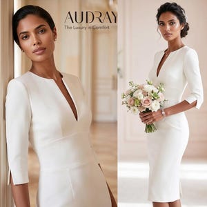 May include: A white knee-length dress with a V-neckline and three-quarter sleeves. The dress features a tailored fit and a slit at the sleeve. The image includes the text "AUDRAY The Luxury in Comfort".