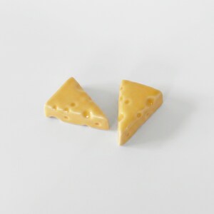 Puede incluir: Dos cuñas triangulares de queso amarillo con agujeros, sobre un fondo blanco. El queso parece cheddar, con un acabado brillante. Las cuñas están separadas, lo que sugiere un tema de comida. Cada cuña mide unos 5 cm de largo.