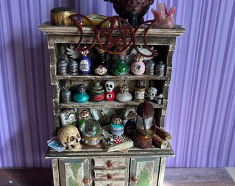 May include: A miniature wooden cabinet with a double door and drawers, filled with potion bottles, skulls, and other witchy items. The cabinet is decorated with a pentagram and moon phases.