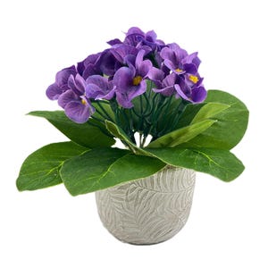 Può includere: Una pianta artificiale in vaso con fiori viola e foglie verdi. Il vaso è bianco con un motivo a foglie.