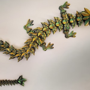 May include: A green and gold origami dragon sculpture. The dragon is made of paper and has a long, serpentine body with a pointed head and tail.
