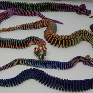 May include: Five iridescent, segmented, plastic snakes with colorful, detailed heads. The snakes are arranged in a semi-circle on a white background.