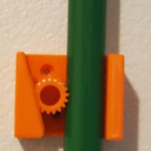 Peut inclure: Support mural en plastique orange avec un tuyau vert attaché. Le support a un petit bouton en forme d'engrenage pour serrer le tuyau.