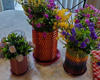 May include: Three colorful, spiky, decorative planters with artificial flowers. The planters are orange, pink, and rainbow colored. The flowers are yellow, purple, and pink.