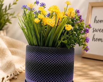May include: A 3D-printed planter pot with a modern design, featuring a dark purple lattice pattern. The pot holds vibrant yellow, purple, and green artificial flowers. Text on the image reads "3D Printed Planter Pot" and "Made to Order."