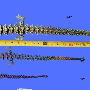 May include: Three origami lizards of different sizes, measuring 12 inches, 18 inches, and 24 inches. The lizards are made of paper and have a green, gold, and purple color scheme.