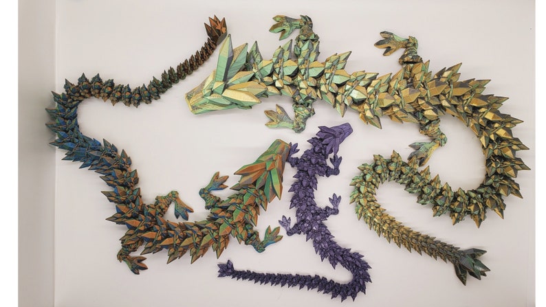 May include: Five origami dragons made of paper with iridescent scales in shades of green, gold, and purple. The dragons are arranged in a decorative display.