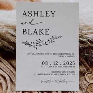 May include: A wedding invitation with a simple design featuring the names Ashley and Blake, the date 08.12.2025, and the text "Joyfully invite you to the celebration of their marriage." The invitation is printed on white cardstock and has a decorative border of leaves.