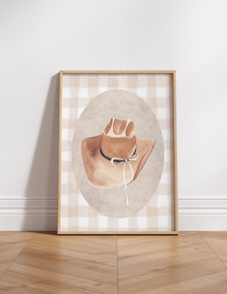 May include: A framed print of a brown cowboy hat with a white ribbon on a gingham background.
