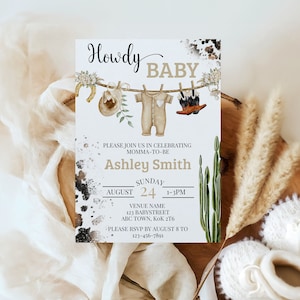 May include: A white baby shower invitation with a rustic western theme. The invitation features a line of clothes hanging on a clothesline with a cowboy hat, baby onesie, and cowboy boots. The text on the invitation reads "Howdy Baby" and includes the name "Ashley Smith" and details for the baby shower.
