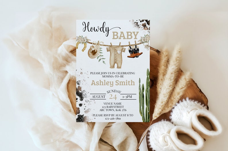 May include: A white baby shower invitation with a rustic western theme. The invitation features a line of clothes hanging on a clothesline with a cowboy hat, baby onesie, and cowboy boots. The text on the invitation reads "Howdy Baby" and includes the name "Ashley Smith" and details for the baby shower.