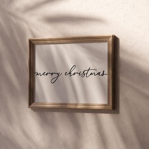 May include: A gold-framed picture with a white background and the text "merry christmas" written in black cursive.