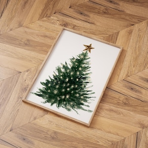 May include: A framed watercolor painting of a green Christmas tree with a gold star on top. The tree is surrounded by white space and the background is a light wood floor.
