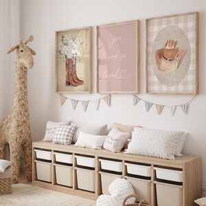 May include: Three framed prints with a pink and white color scheme. The prints feature a pair of cowboy boots with flowers, a pink background with the text "you were so loved", and a brown cowboy hat on a white and brown gingham background.