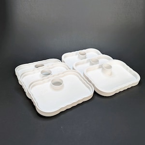 May include: Set of six white plastic trays with a raised center circle. The trays are designed to hold small items, such as candles or soap.