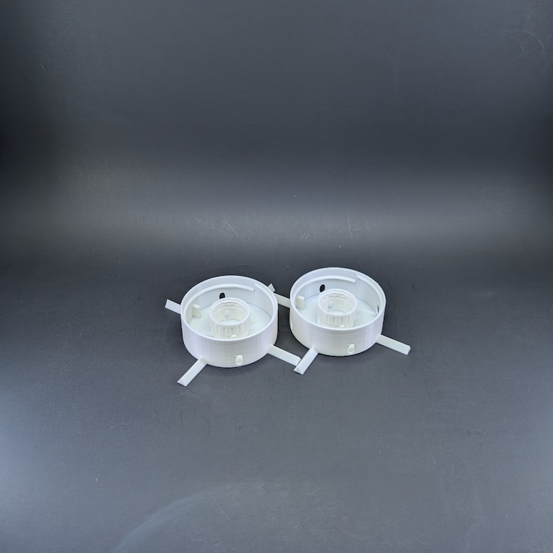 May include: Two white plastic light fixture bases with three prongs each. The bases are designed to hold light bulbs.