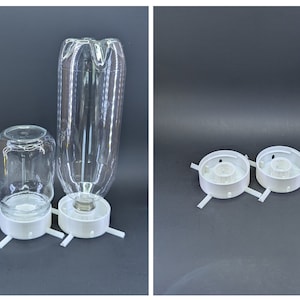 May include: Two white plastic bases with four arms each, designed to hold glass jars or bottles. One base is holding a clear glass jar and the other is holding a clear plastic bottle.