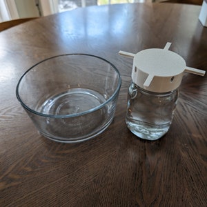 May include: A clear glass bowl and a clear glass jar with a white plastic lid. The lid has four arms that extend out from the centre.