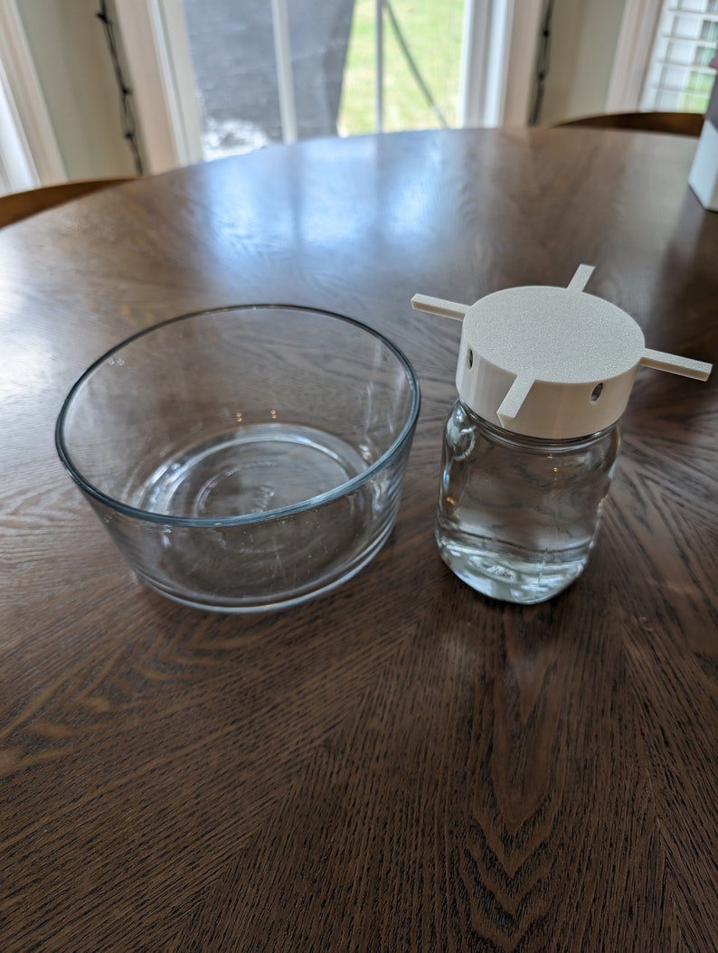 May include: A clear glass bowl and a clear glass jar with a white plastic lid. The lid has four arms that extend out from the centre.