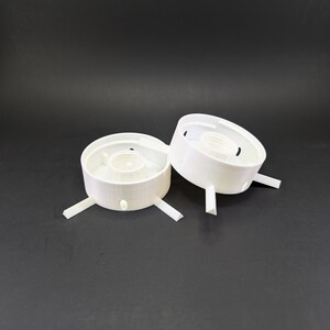 May include: Two white plastic lamp holders with three prongs each. The holders have a circular base and a central opening for a light bulb.