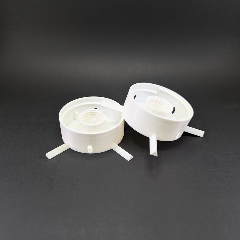 May include: Two white plastic lamp holders with three prongs each. The holders have a circular base and a central opening for a light bulb.