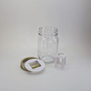 May include: A clear glass jar with a gold lid and a white plastic lid with a square opening. The jar is empty and the lids are separate.