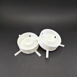 May include: Two white plastic electrical outlet covers with four prongs each. The covers are designed to be mounted on a wall or ceiling.