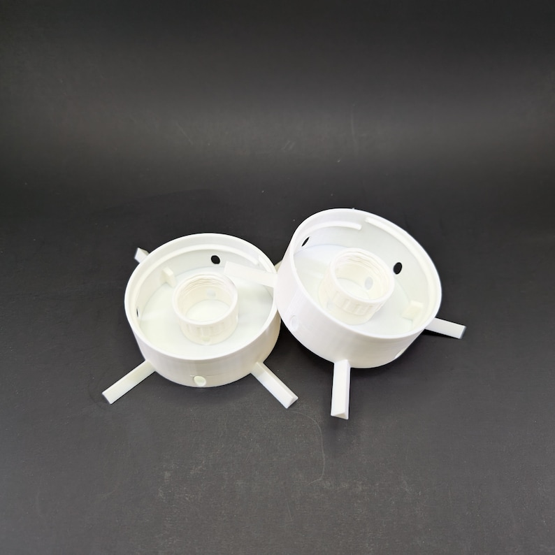 May include: Two white plastic electrical outlet covers with four prongs each. The covers are designed to be mounted on a wall or ceiling.