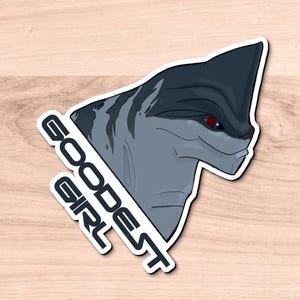 Puede incluir: Una pegatina con una criatura de dibujos animados gris y azul con un ojo rojo. La pegatina tiene el texto "goodest girl" escrito en diagonal.
