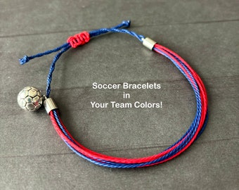 May include: A soccer bracelet with red and blue cords, and a silver soccer ball charm. The bracelet has a sliding knot closure. The text on the image reads: "Soccer Bracelets in Your Team Colors!"