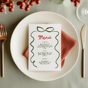 May include: A white menu card with a green ribbon design and the word "Menu" in red. The menu lists starters, main courses, and desserts, including Goat Cheese and Cranberry Crostini, and Maple Glazed Ham.