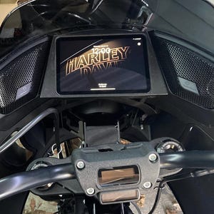 May include: Black motorcycle dashboard featuring a digital display with the Harley-Davidson logo and time. The dashboard includes speakers and a handlebar with controls. The design is sleek and modern.