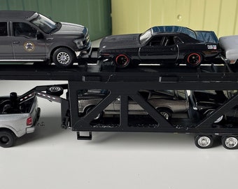 Pode incluir: Uma camioneta prateada rebocando um transportador de carros preto com quatro carros nele. Os carros no transportador são um carro de músculo preto, um carro de músculo prateado, um sedan preto e um sedan prateado.