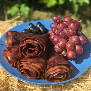 Peut inclure: Une assiette bleue pr&eacute;sente des rouleaux de cuir de fruits, des raisins noirs et des raisins rouges. Le cuir de fruits est brun fonc&eacute;, roul&eacute; en spirales. Les raisins sont d'un rouge profond et noir, cr&eacute;ant une pr&eacute;sentation color&eacute;e et app&eacute;tissante.