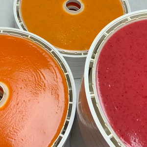 Peut inclure: Gros plan sur trois plateaux remplis de cuir de fruits aux tons orange et rouge. Les plateaux blancs ont un trou central circulaire et sont empil&eacute;s. Le cuir de fruit semble lisse et uniform&eacute;ment r&eacute;parti.