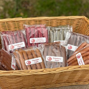 Peut inclure: Un panier en osier rempli de rouleaux de fruits secs emball&eacute;s individuellement. Les saveurs incluent Pomme Grenade, Antivitus Cranberry Lemon Honey Ginger Apple et Fraise Pomme. Les &eacute;tiquettes ont un logo de pomme rouge.