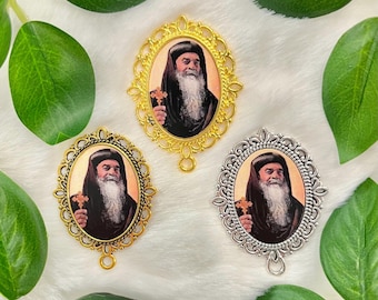 Op de afbeelding: Drie ovale hangers met sierlijke gouden en zilveren frames. Elke hanger toont een portret van een man met een lange witte baard en een zwarte robe. De man houdt een kruis in zijn rechterhand.