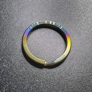 May include: A metal keychain ring with a rainbow iridescent finish. The ring has the engraved text "A DAD BOD IS A RAD BOD". The ring is split at one point, allowing it to be opened and closed.