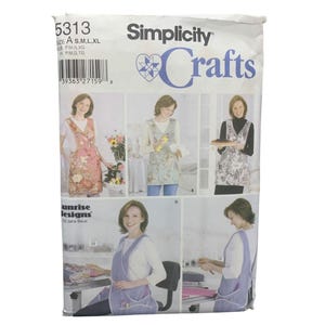 May include: Simplicity Crafts sewing pattern featuring apron designs. The pattern includes various apron styles with floral and solid color options. The package shows different apron variations, with sizes A, S, M, L, and XL.